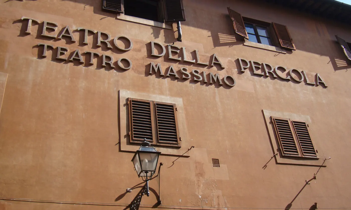 The ochre wall of the Teatro della Pergola in Florence, with its name in raised letters, wooden shutters and a street lamp