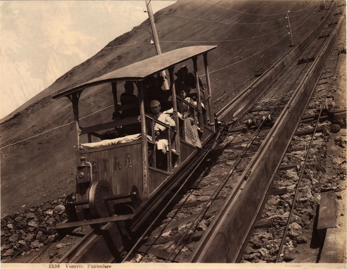 A sepia photograph of a funicular car climbing a steep track on the slope of Mount Vesuvius, with people seated inside