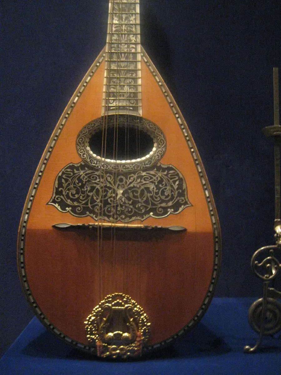 A bowl-backed Neapolitan mandolin with a decorated metal soundboard and tortoiseshell guard, displayed against a dark blue ground
